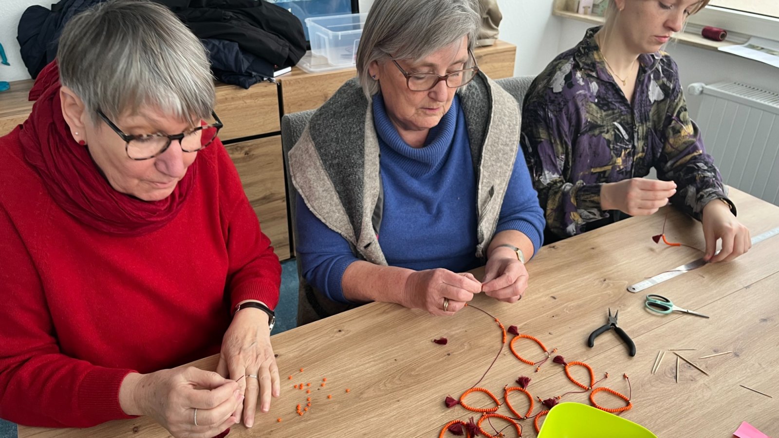 SkF Vorständinnen beim Fertigen von Armbändern aus orangenen Glasperleb