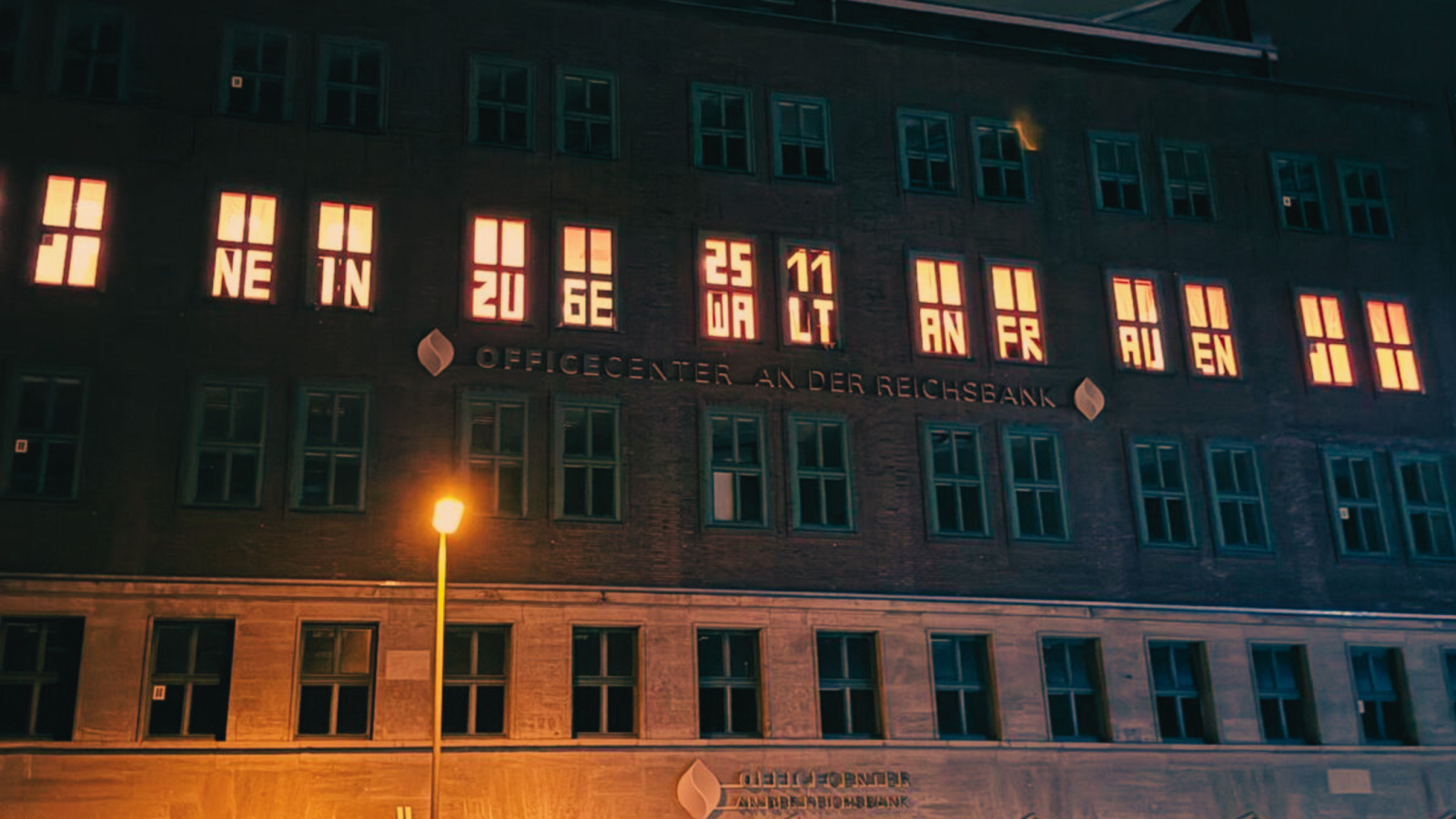 Beleuchtete Fensterfront der Zentrale mit dem Schriftzug Nein Zu Gewalt an Frauen