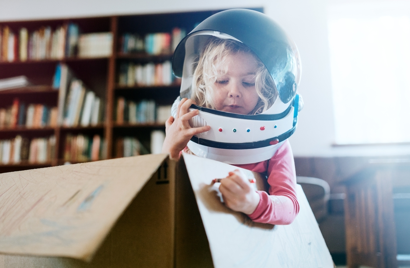 Mädchen im Pappkarton mit Astronautenhelm auf dem Kopf