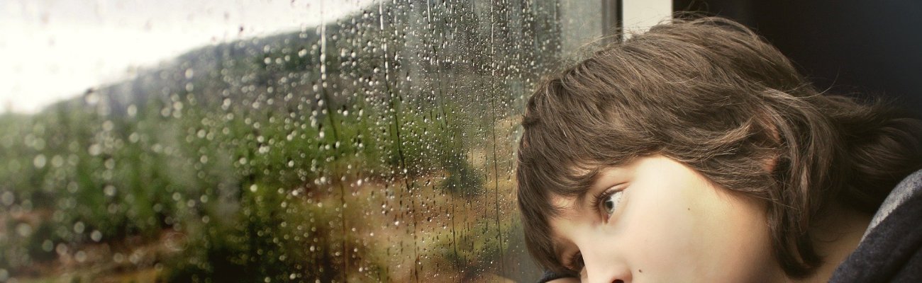 Junge schaut traurig aus Fenster